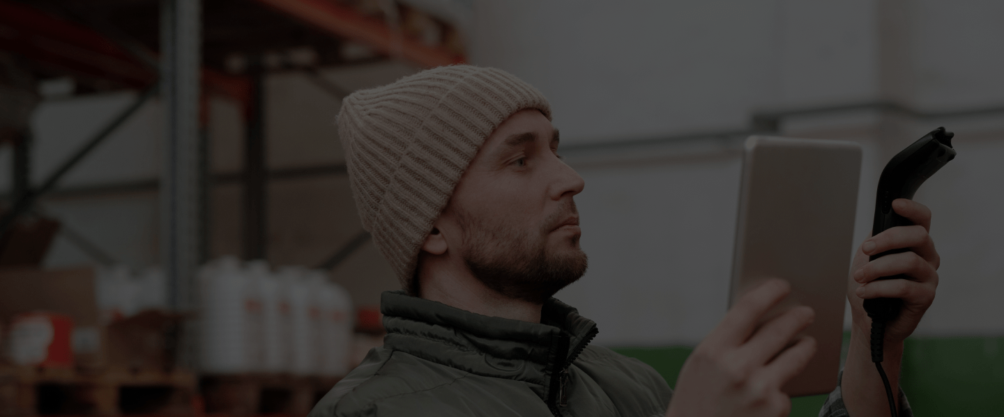 A man in a beanie looking at their barcode scanner while holding a tablet