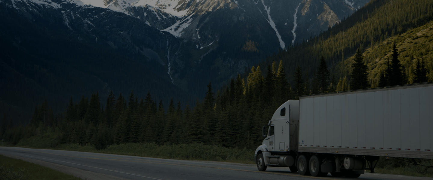 A side view of a truck driving past a forest and mountains