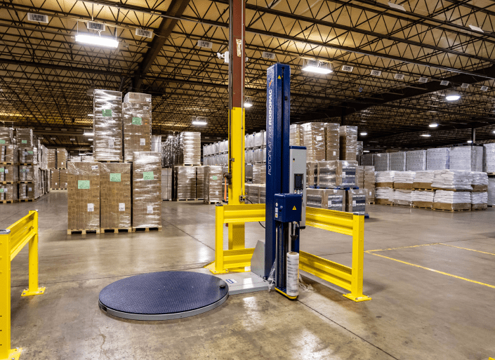 A stretch wrap machine in front of stacked pallets in a warehouse