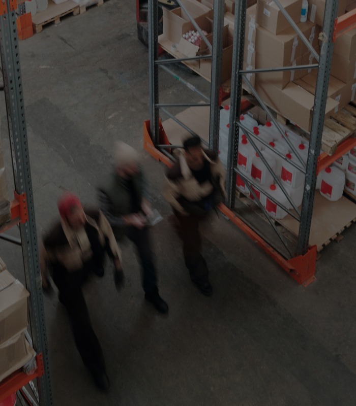 Three men walking quickly down an aisle in a warehouse